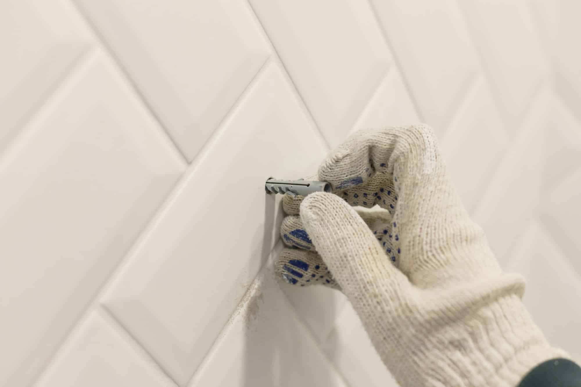 Worker's hand in glove inserts wall pvc dowel in wall cladded with tile ceramic